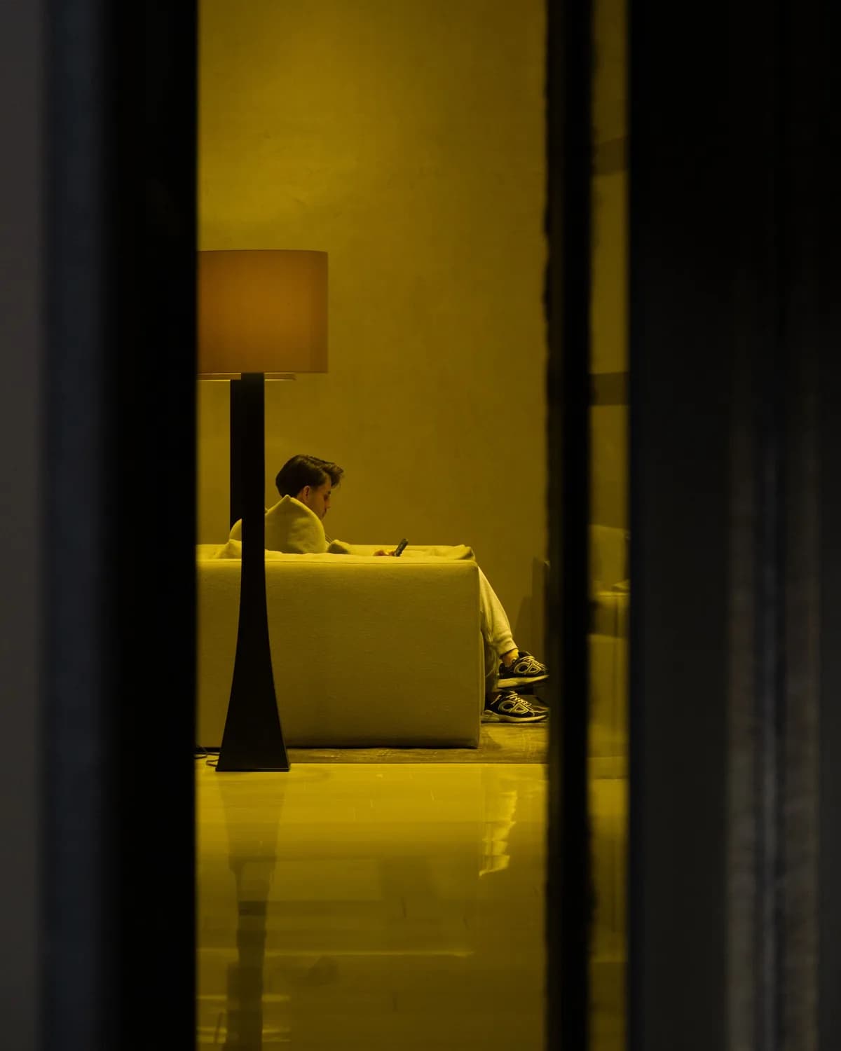 Pessoa em casa à noite, sentada no sofá sob a luz do abajur, com o celular na mão