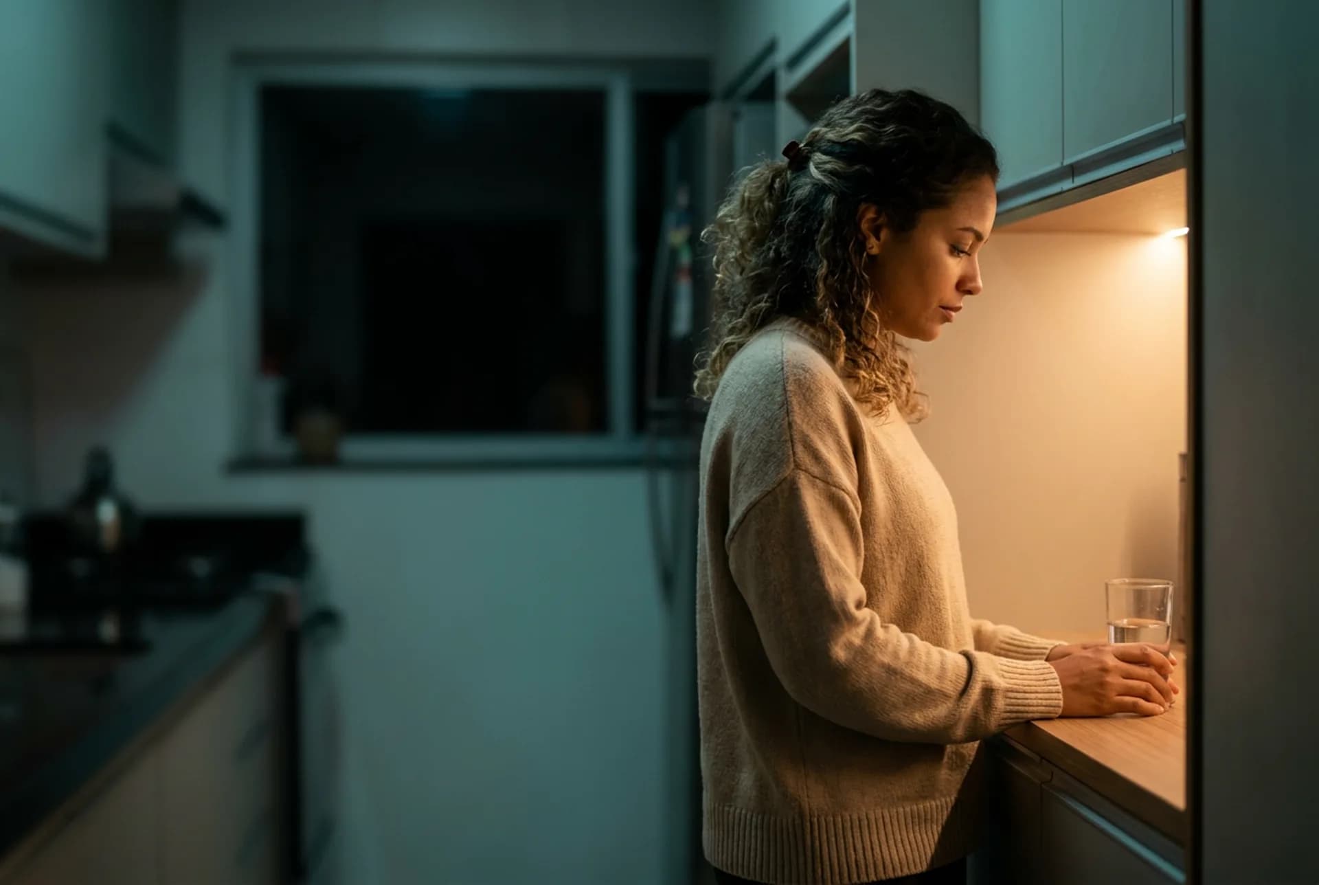 Balcão de cozinha à noite com armário fechado e copo d’água — pausa emocional